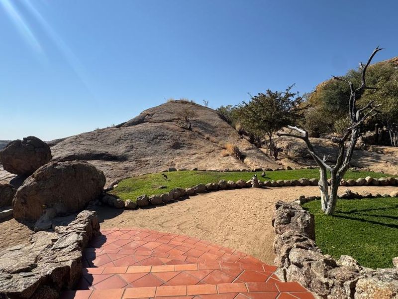 A beautifully landscaped garden area featuring natural rock formations, manicured lawn, stone retaining walls, and terracotta tiled steps leading into the outdoor space.