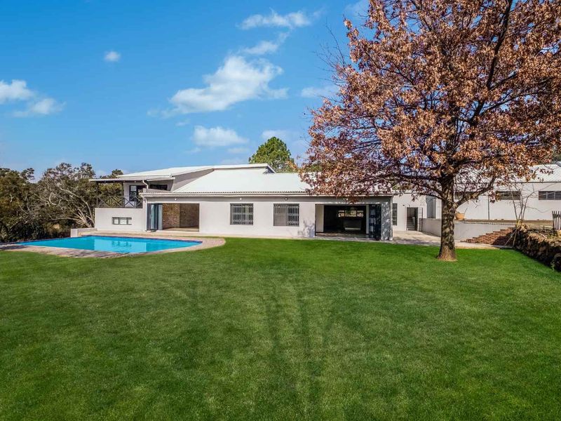 Rear view of the property featuring a well-maintained lawn, a swimming pool, and a modern home with large folding glass doors.