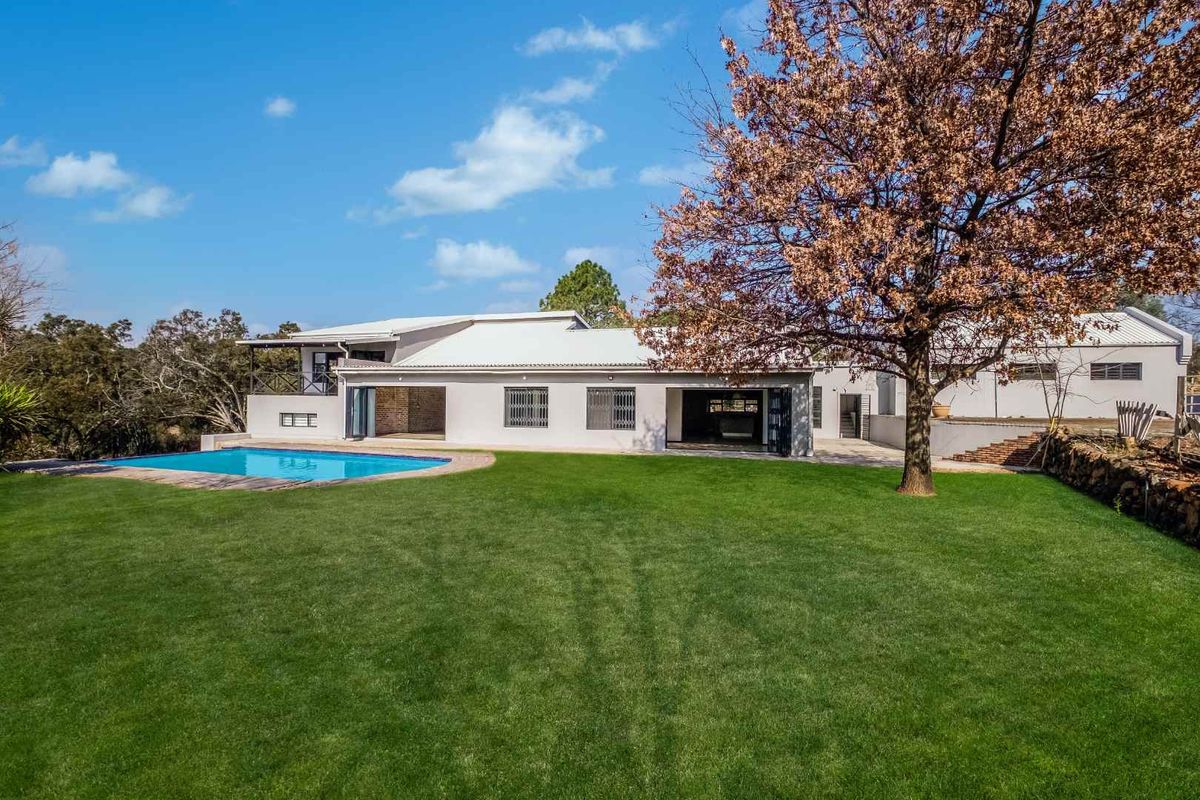 Rear view of the property featuring a well-maintained lawn, a swimming pool, and a modern home with large folding glass doors.