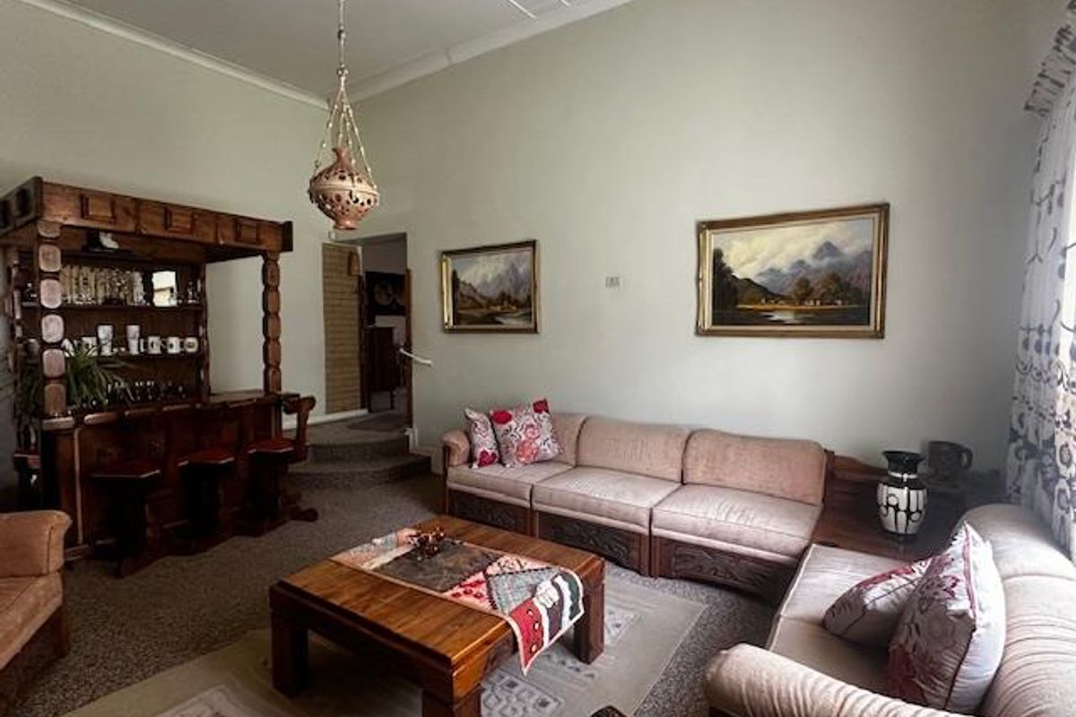 A spacious living room featuring a built-in wooden bar unit, high ceilings, and carpeted flooring, offering a traditional layout with potential for modernization.