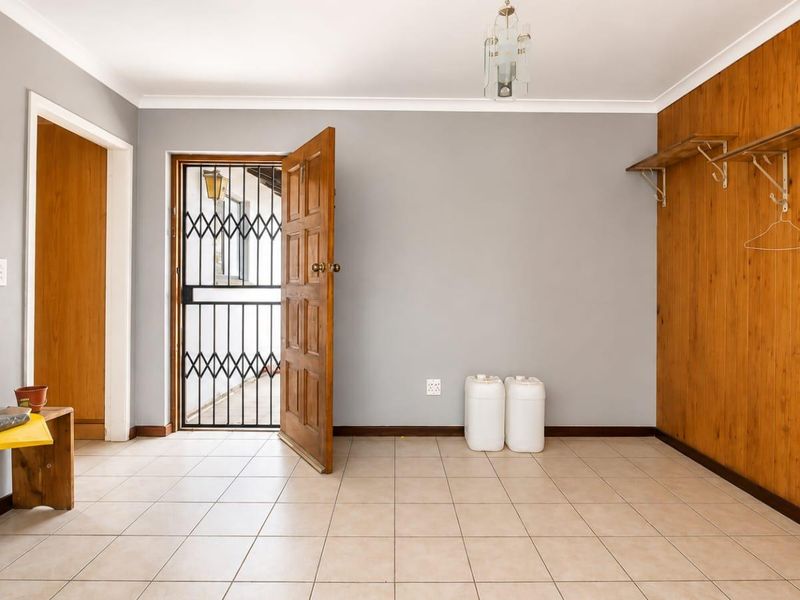 An entry area featuring tiled flooring, a security gate, and a feature wall with timber paneling and built-in shelving.