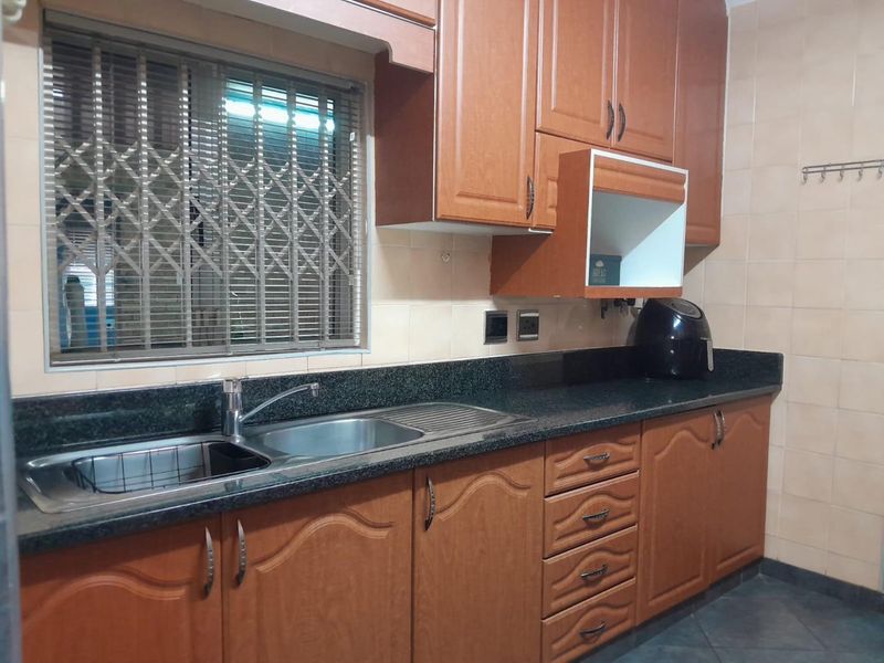A functional kitchen featuring wood-finish cabinetry, granite countertops, a stainless steel sink, and tiled backsplash with a secure window.