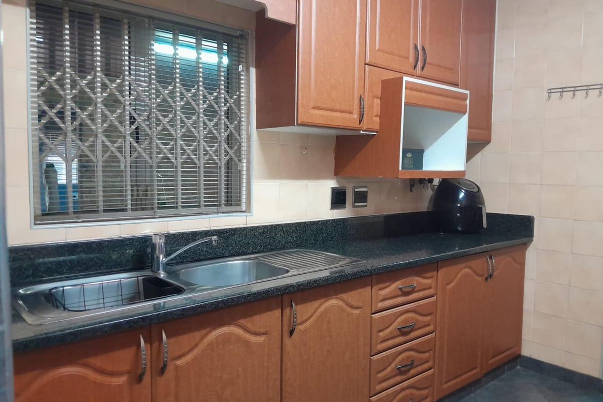 A functional kitchen featuring wood-finish cabinetry, granite countertops, a stainless steel sink, and tiled backsplash with a secure window.