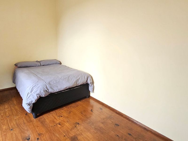 A simple bedroom featuring timber flooring and plain painted walls, offering a blank canvas for potential interior updates.