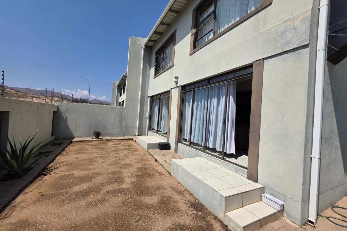 Rear view of the townhouse featuring a paved patio area, sliding glass doors, and a private garden space with perimeter wall and electric fencing.