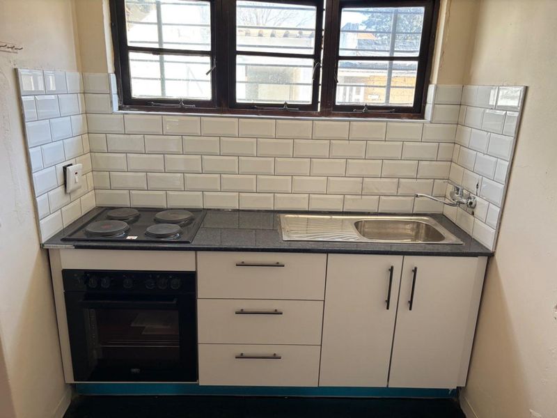 Compact kitchen featuring a granite countertop, subway tile backsplash, built-in electric oven and hob, and stainless steel sink with window security bars.