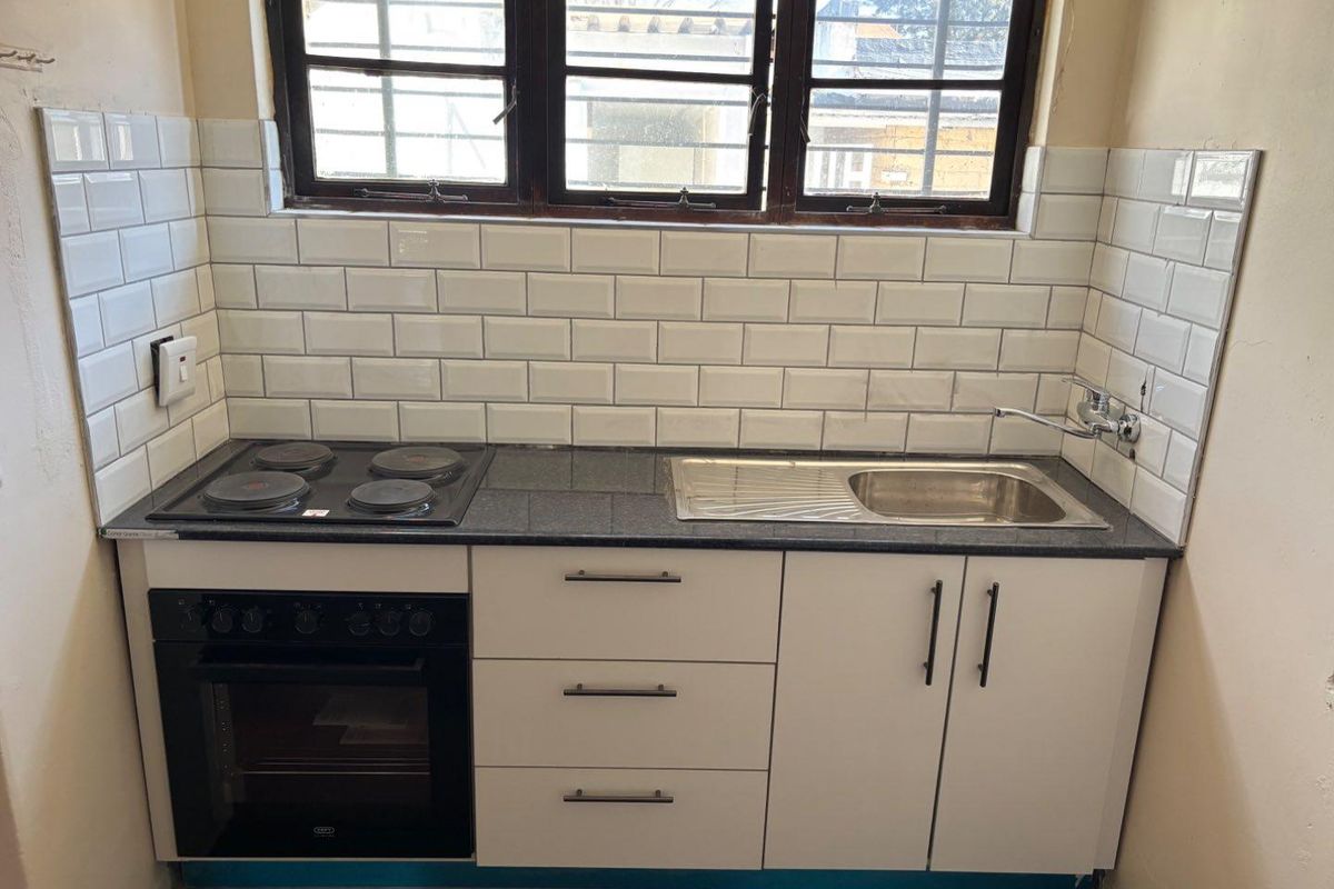 Compact kitchen featuring a granite countertop, subway tile backsplash, built-in electric oven and hob, and stainless steel sink with window security bars.