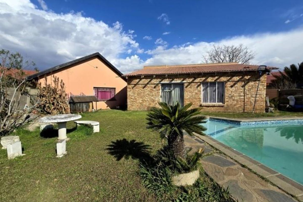 Rear view of the property featuring a brick facade, swimming pool, and garden area with established landscaping.