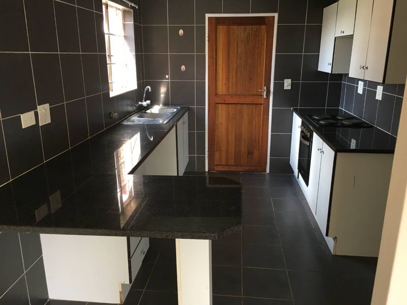 A functional kitchen featuring dark tiled walls, granite countertops, built-in oven, electric hob, and ample storage cabinetry.