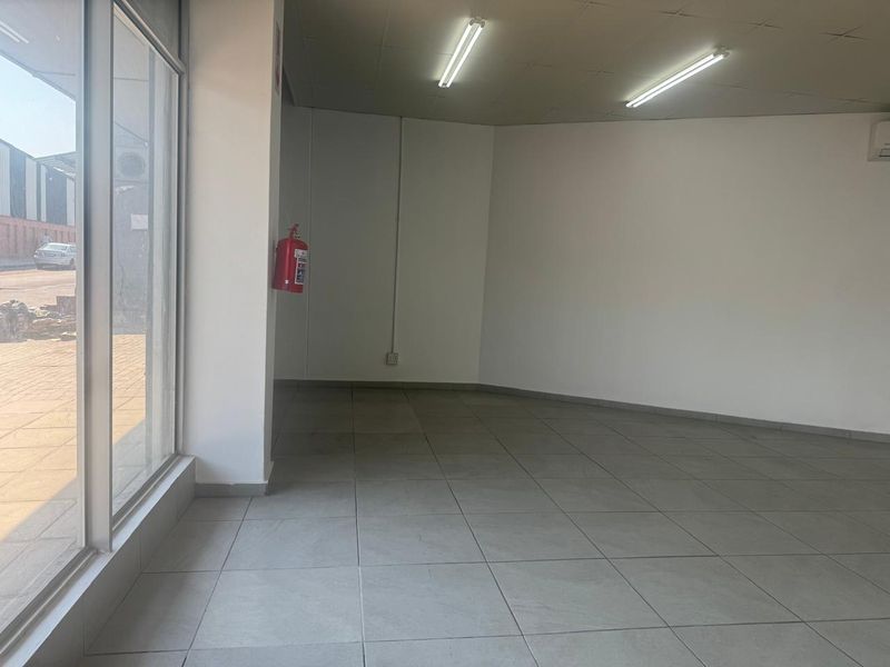 A bright, empty open-plan retail space featuring large glass storefront windows, tiled flooring, and functional overhead lighting, suitable for various commercial business applications.