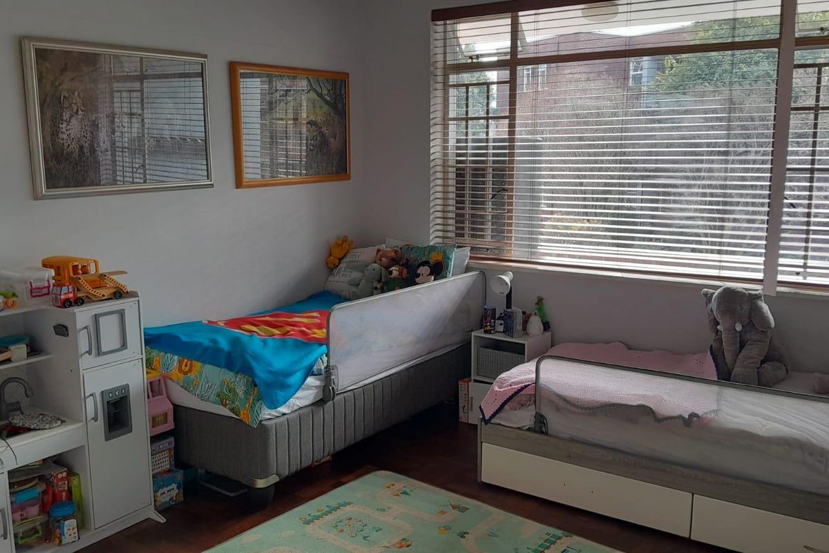 A functional bedroom featuring laminate flooring and large windows fitted with venetian blinds, providing ample natural light.