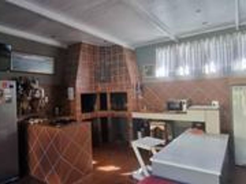 Covered patio area featuring a large built-in brick braai, tiled finishes, and ample space for outdoor entertaining.