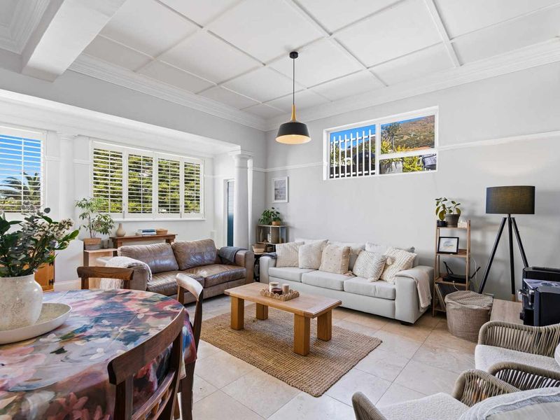 Spacious open-plan living and dining area featuring elegant coffered ceilings, crown molding, tiled flooring, and plantation shutters for natural light control.