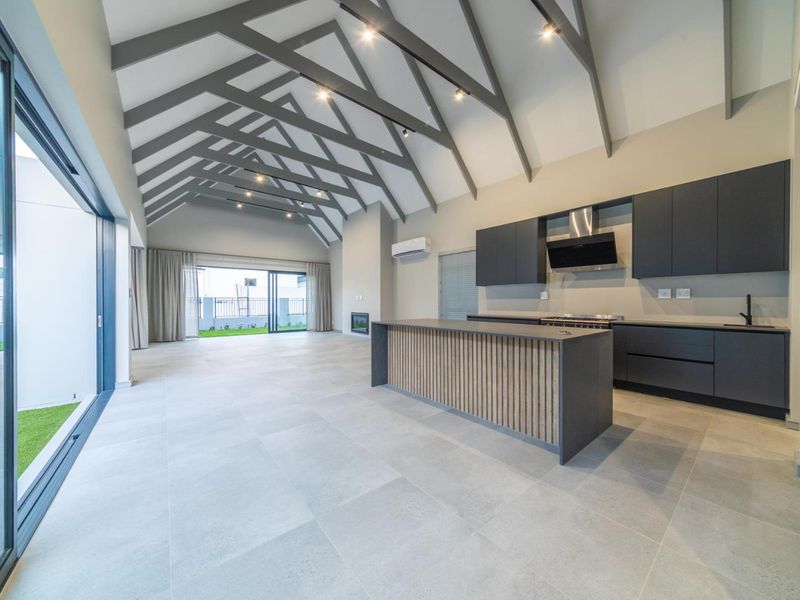 Spacious open-plan living area featuring a modern kitchen with island, vaulted ceilings with exposed rafters, and large sliding doors leading to the garden.