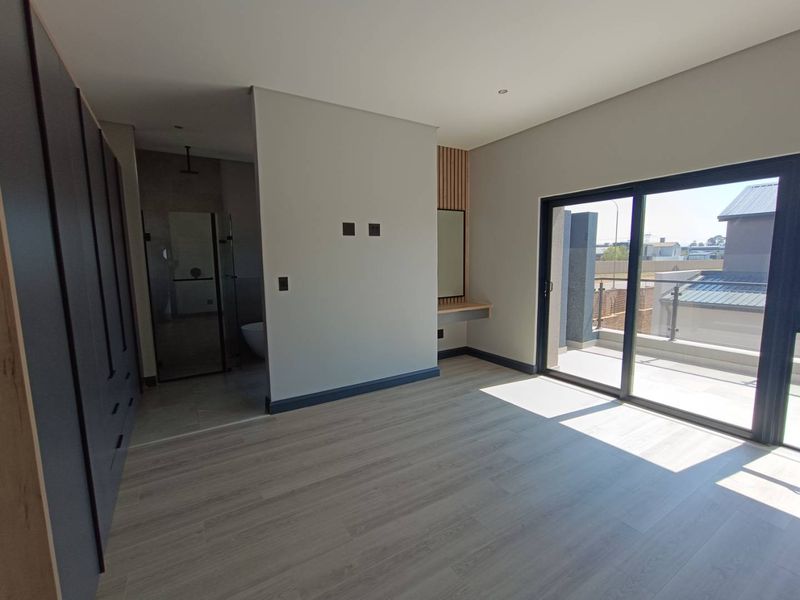 Modern bedroom featuring laminate flooring, built-in cupboards, a floating vanity, and a sliding glass door leading to a private balcony.