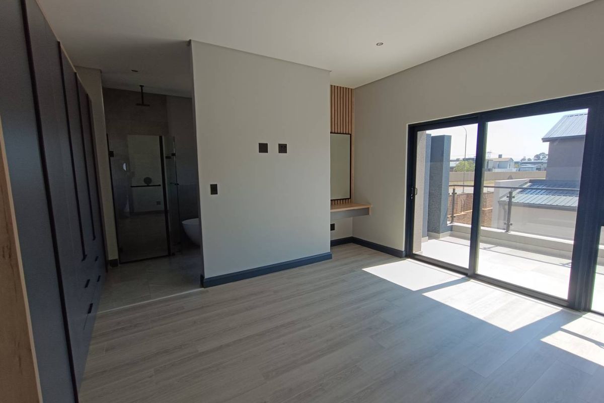 Modern bedroom featuring laminate flooring, built-in cupboards, a floating vanity, and a sliding glass door leading to a private balcony.