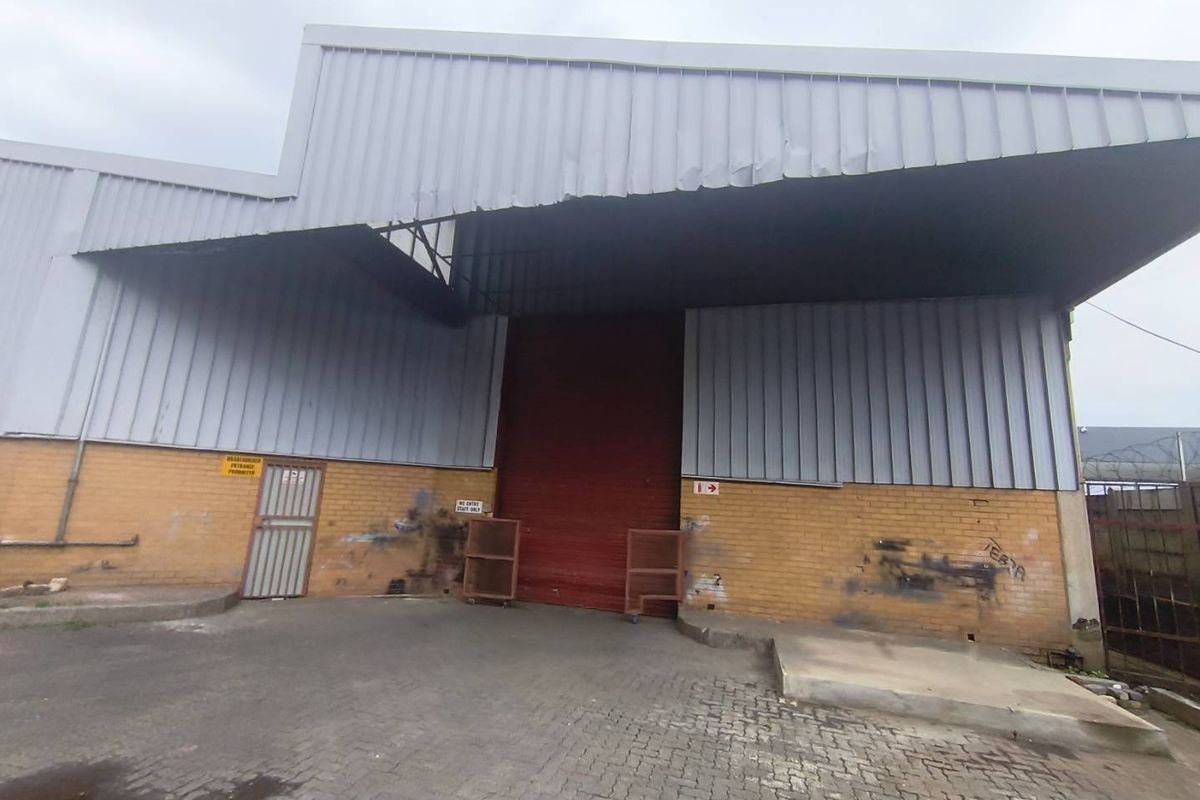 Industrial warehouse exterior featuring a large roller shutter door, corrugated metal cladding, and paved driveway access.