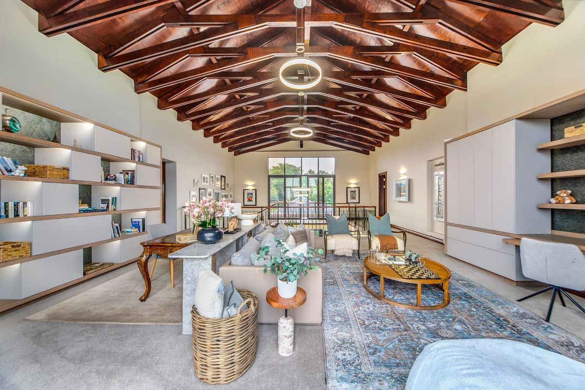Spacious living area featuring a dramatic vaulted timber-beamed ceiling, integrated custom cabinetry, and large windows providing natural light and garden views.