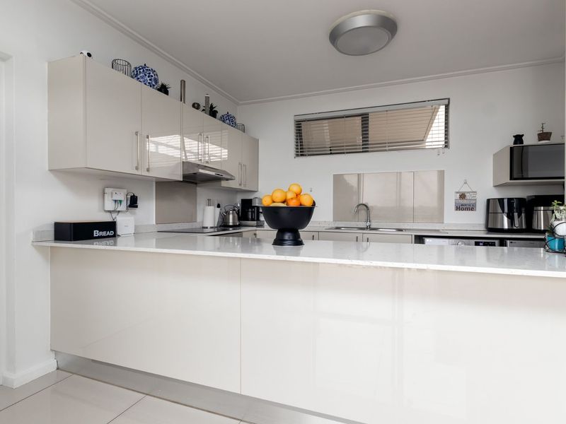 Modern kitchen featuring high-gloss cabinetry, stone countertops, integrated appliances, and tiled flooring, offering a clean and functional workspace.