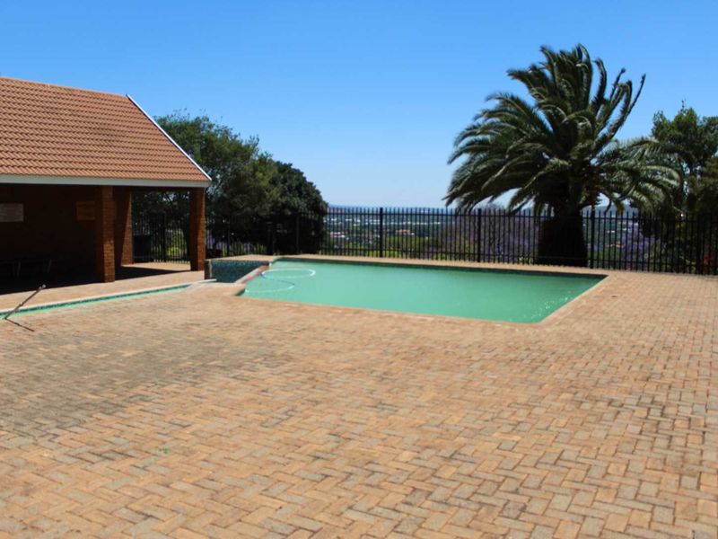 Communal pool area featuring brick paving, a covered patio structure, and metal perimeter fencing with scenic views.