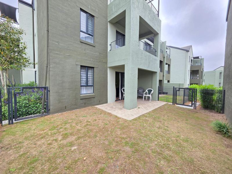Ground floor apartment exterior featuring a paved patio area, private garden space, and secure metal fencing.