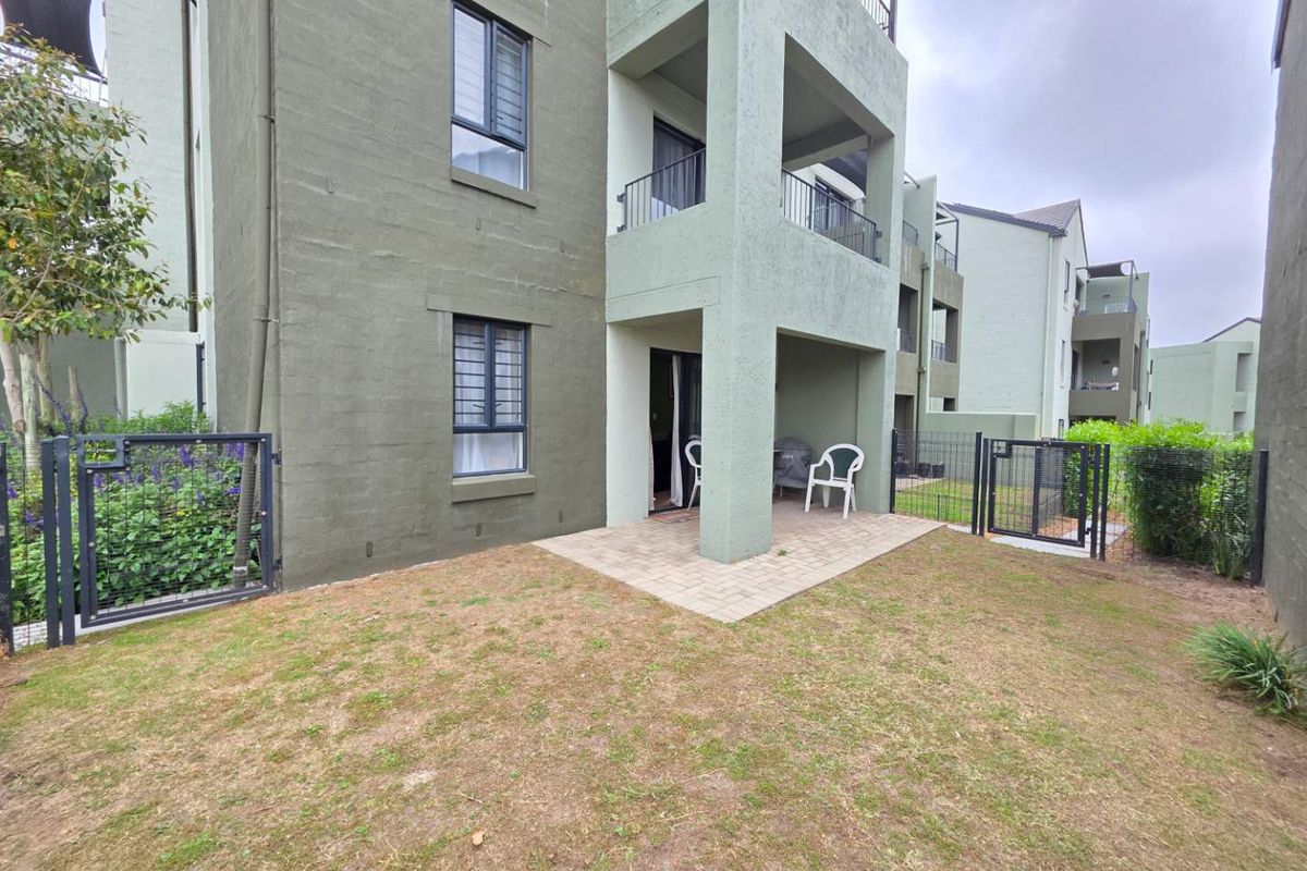 Ground floor apartment exterior featuring a paved patio area, private garden space, and secure metal fencing.