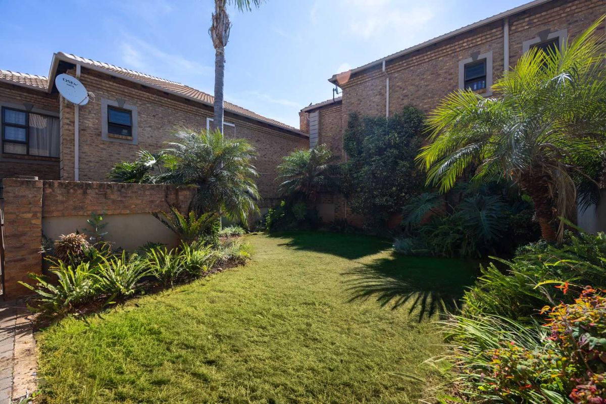 A private rear garden area featuring a well-maintained lawn, established landscaping, and brick townhouse exterior walls.