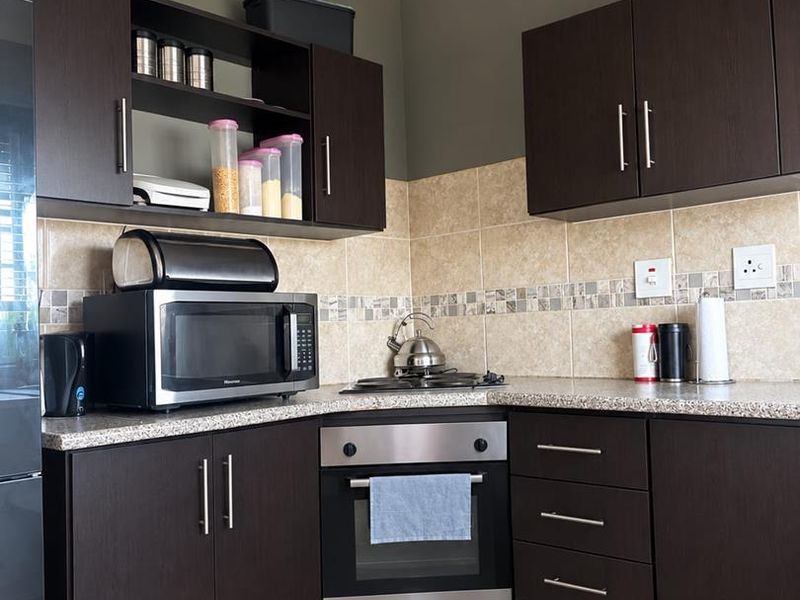 A functional kitchen featuring dark wood cabinetry, granite countertops, a built-in oven, gas hob, and neutral tiled backsplash.