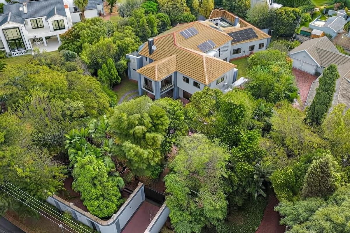 Aerial view of a residential property featuring a tiled roof with solar panels, surrounded by mature trees and a well-maintained garden.