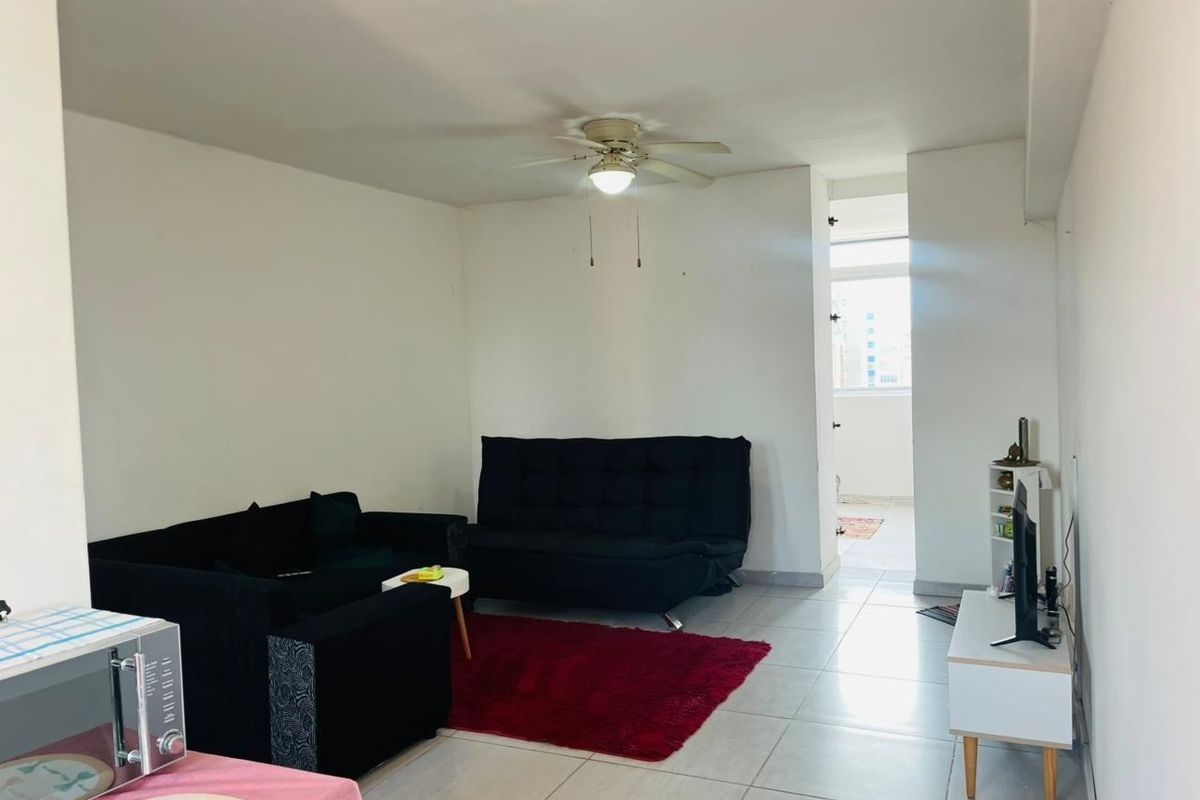 A simple living room area featuring tiled flooring and a ceiling fan, with direct access to an adjacent balcony space.