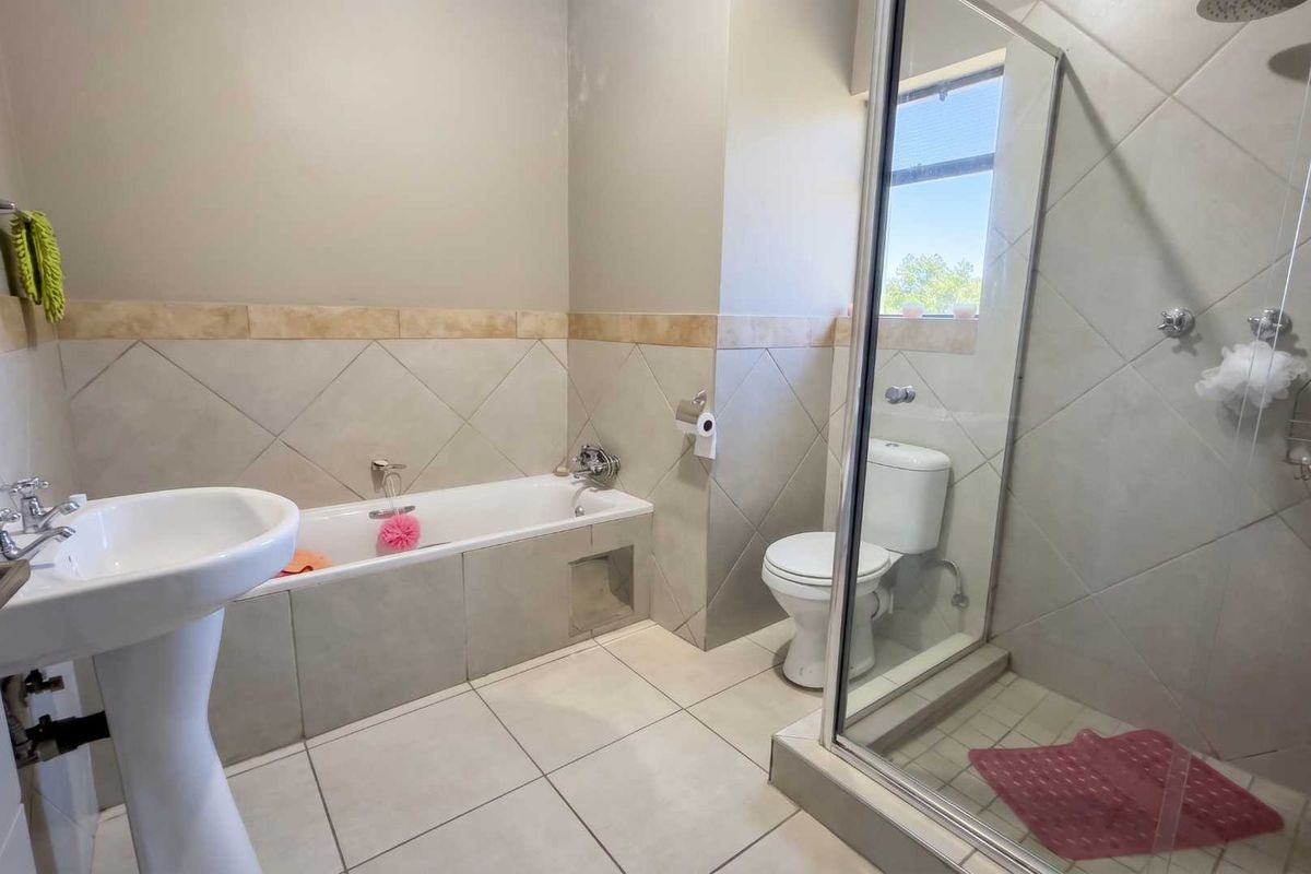 A functional bathroom featuring a pedestal basin, a built-in bathtub, and a separate glass-enclosed shower with neutral wall and floor tiling.
