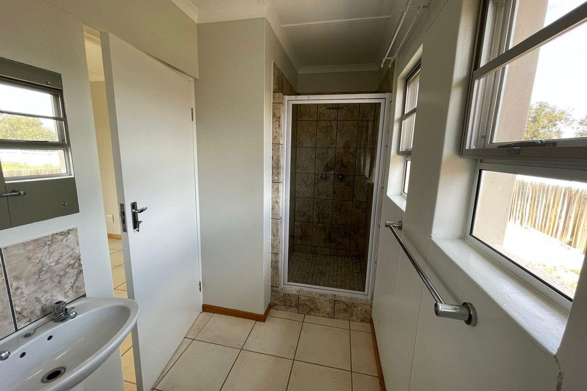 A functional bathroom featuring a tiled shower enclosure, pedestal basin, and large windows providing natural light.