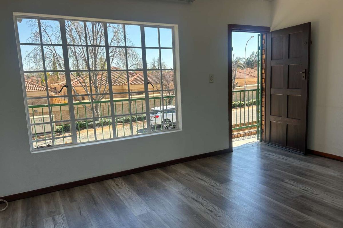 An empty living room featuring modern laminate flooring, a large grid window, and a timber door leading to an exterior balcony area.
