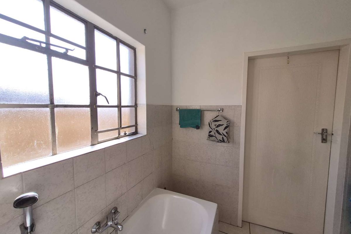 A functional bathroom featuring a built-in bathtub, tiled walls, and a steel-framed window, offering a clean, dated space ready for modernization.
