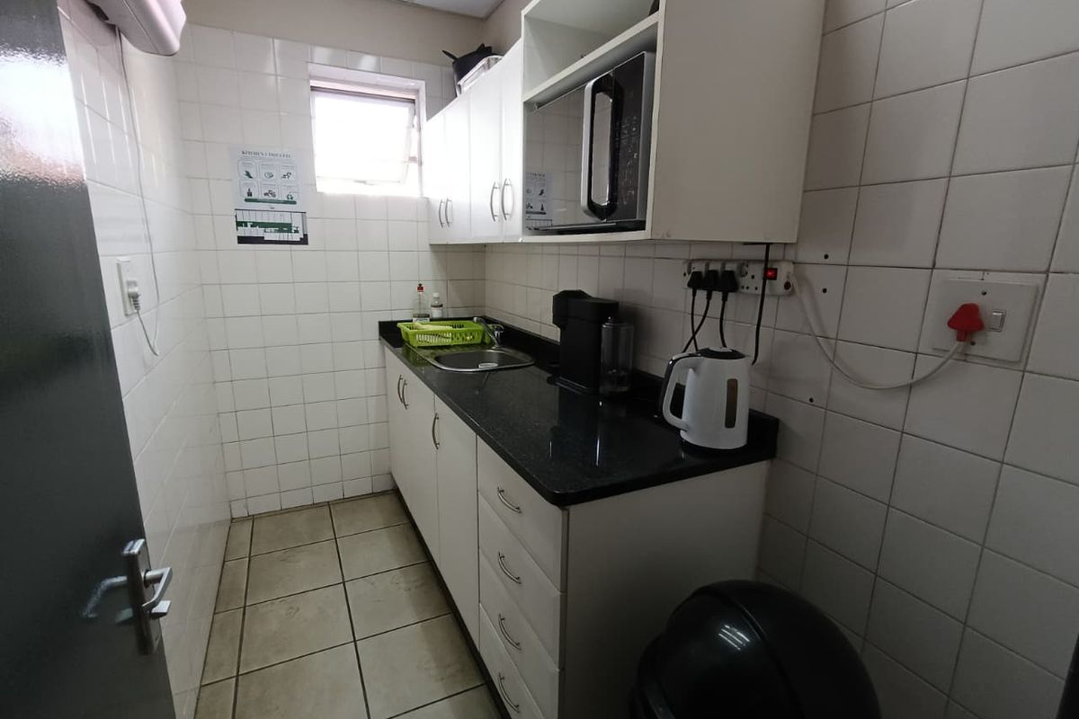 Compact kitchenette featuring white cabinetry, dark granite countertops, a stainless steel sink, and full wall tiling, suitable for office or utility use.