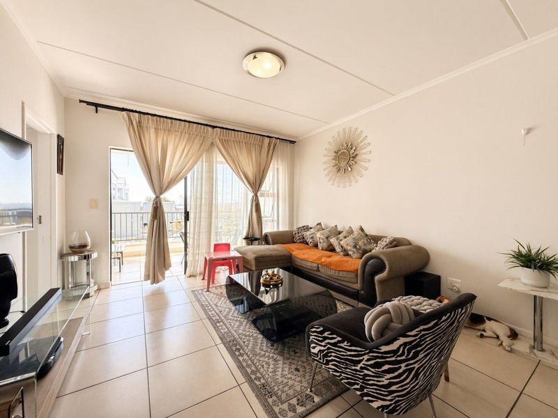 A bright living room featuring tiled flooring and a sliding glass door providing direct access to an outdoor balcony area.