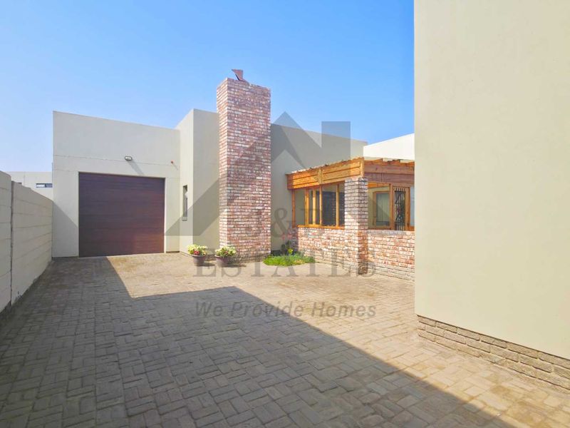 Rear exterior view featuring a paved driveway, brick chimney, and a timber pergola structure attached to the house.
