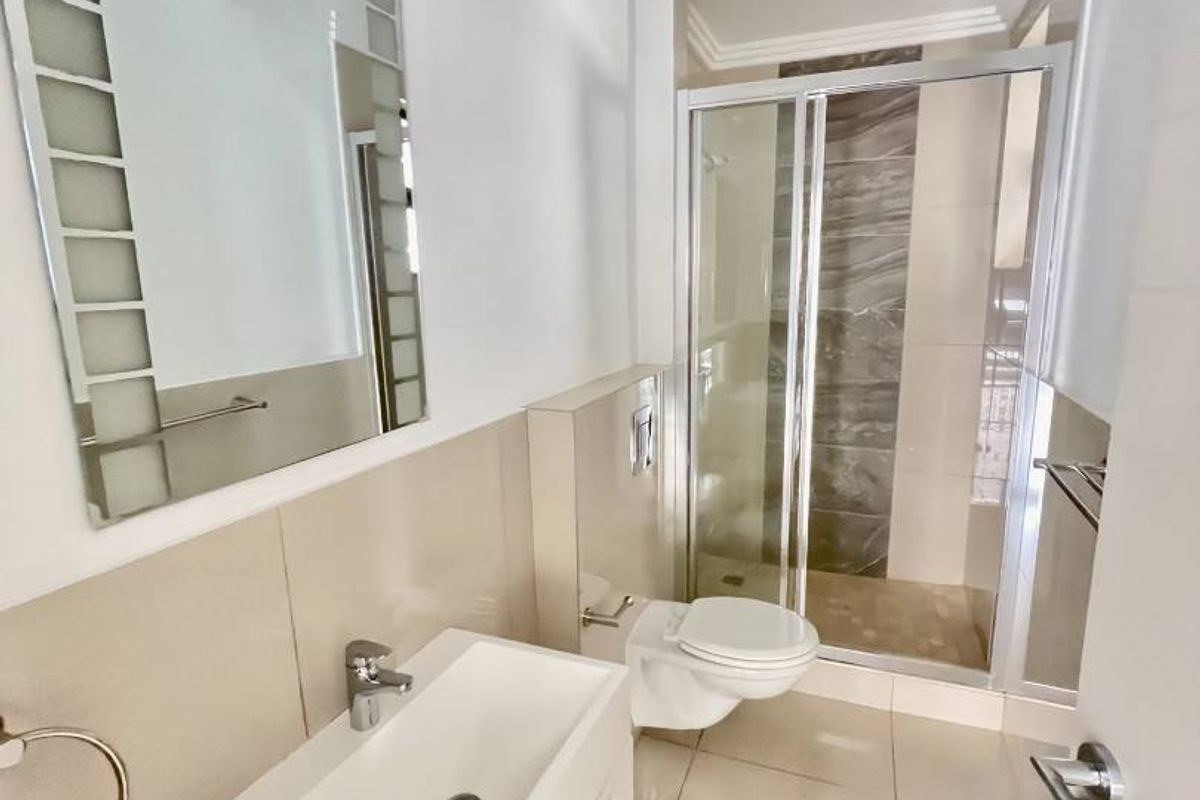 Modern bathroom featuring a wall-mounted vanity, a glass-enclosed shower with tiled accents, and a wall-hung toilet with neutral floor tiling.