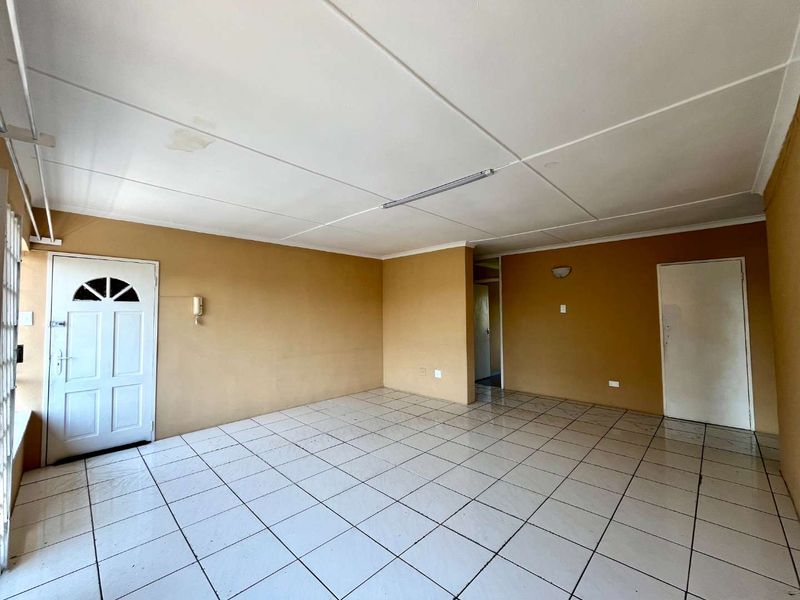 An empty, open-plan living area featuring white tiled flooring, neutral wall paint, and a functional intercom system, ready for renovation or staging.