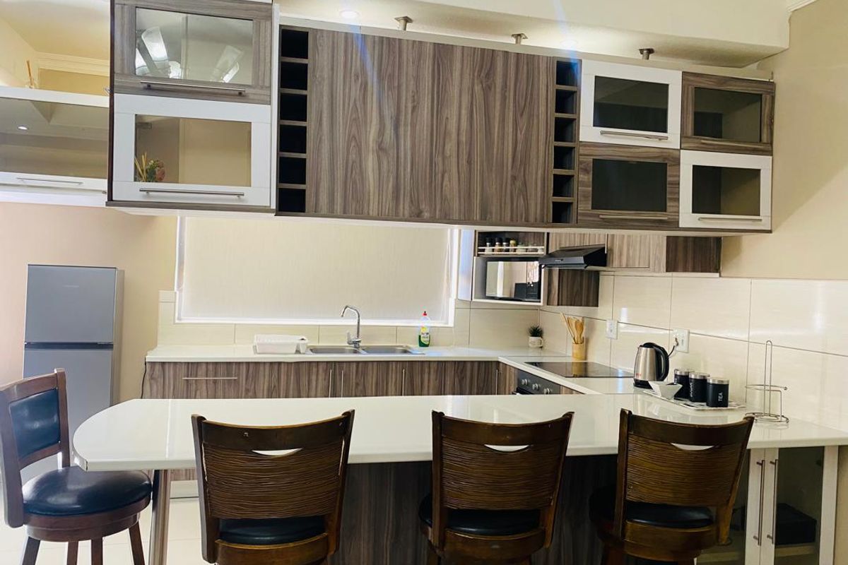 Modern kitchen featuring wood-grain cabinetry, white countertops, a breakfast bar, integrated hob, and tiled backsplash in a well-lit, functional layout.