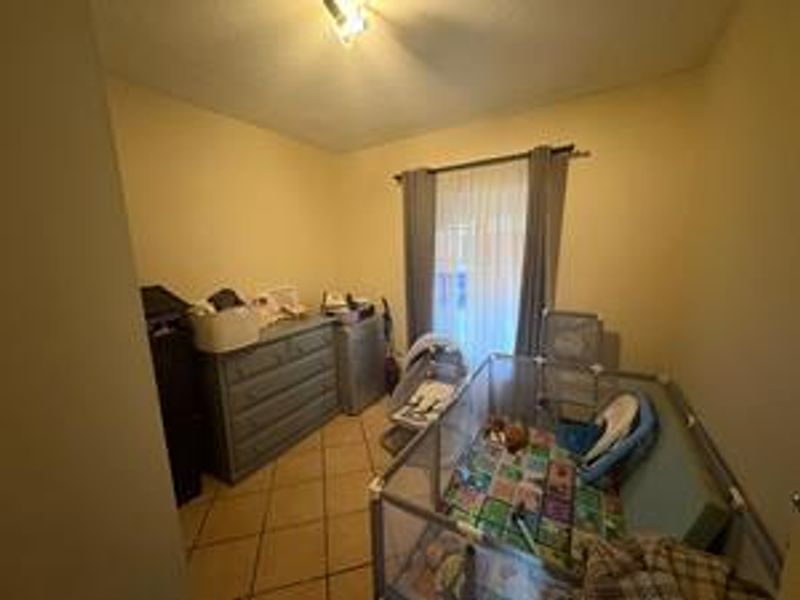 A bedroom featuring tiled flooring and a window with curtain rods, currently utilized as a nursery space.