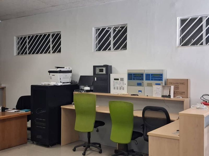 Functional office space featuring built-in desk workstations, integrated fire alarm control panels, and security-barred windows.