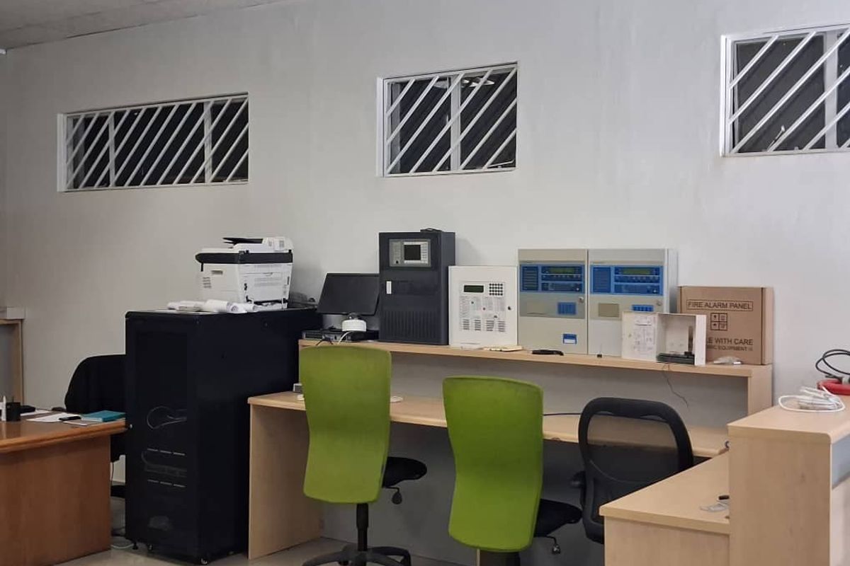 Functional office space featuring built-in desk workstations, integrated fire alarm control panels, and security-barred windows.