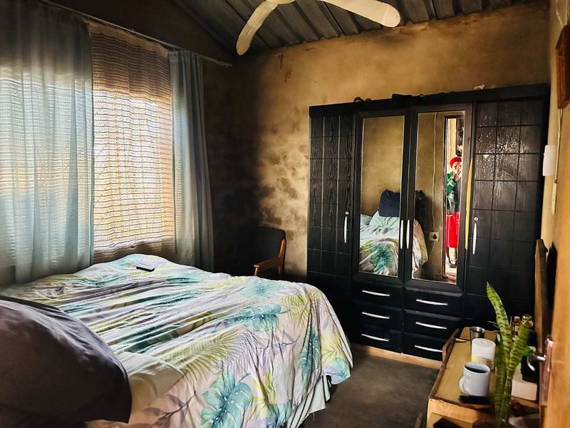 A bedroom featuring an exposed corrugated metal ceiling, ceiling fan, and significant wall surface deterioration requiring maintenance and cosmetic updates.