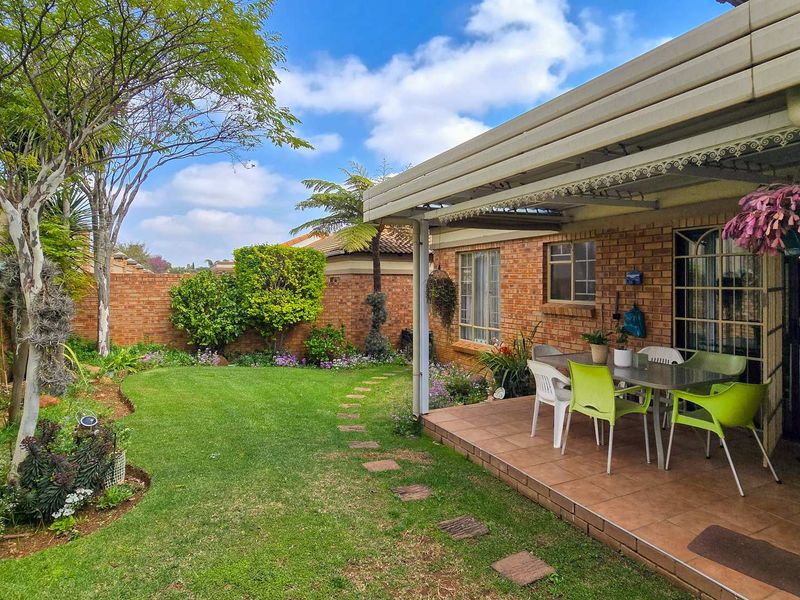 A well-maintained covered patio area featuring tiled flooring, overlooking a private landscaped garden with brick boundary walls.
