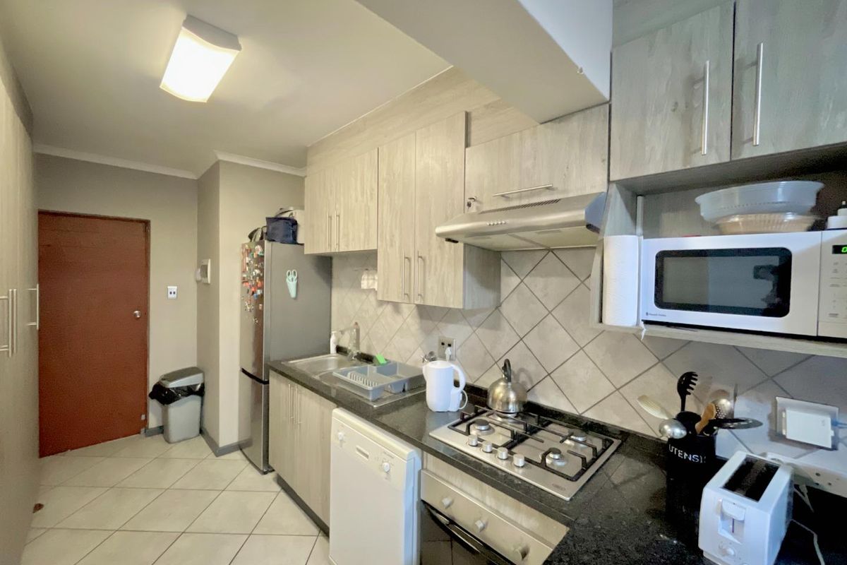 Compact kitchen featuring light wood-grain cabinetry, dark granite countertops, a built-in gas hob, extractor fan, and tiled flooring.