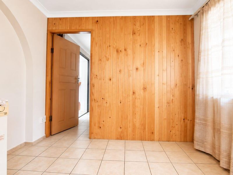 A functional laundry area featuring tiled flooring, timber wall paneling, and an arched entryway leading to the rest of the home.