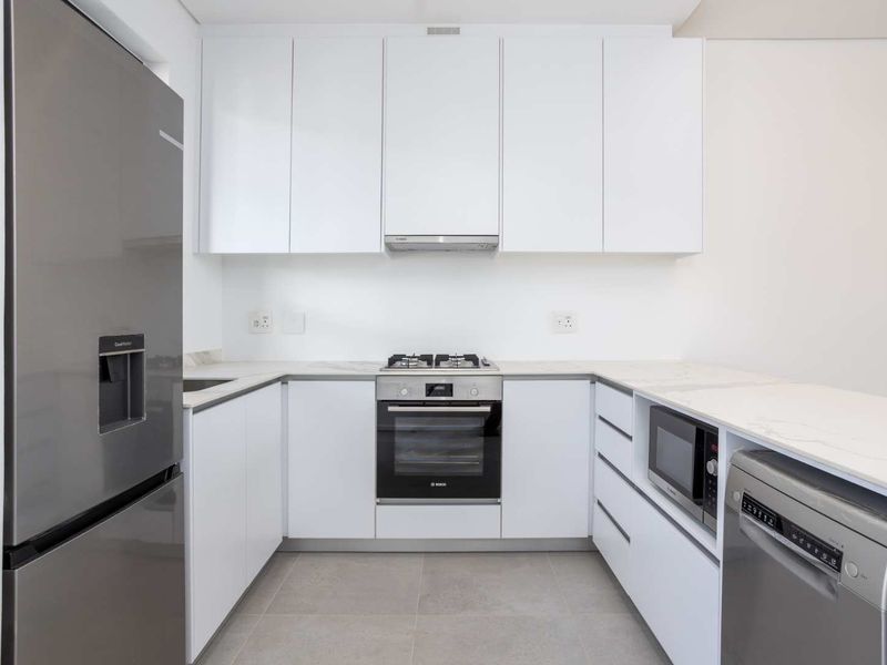 Modern kitchen featuring white cabinetry, stone countertops, integrated appliances including a gas hob, oven, and built-in microwave, with sleek tiled flooring.