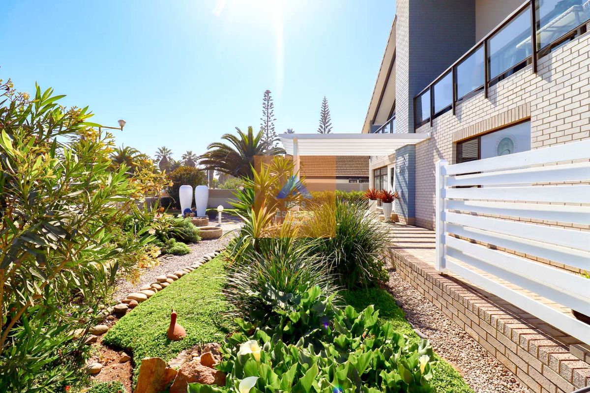 A well-maintained rear garden area featuring landscaped beds, a paved walkway, and a covered patio structure adjacent to the brick-clad house exterior.