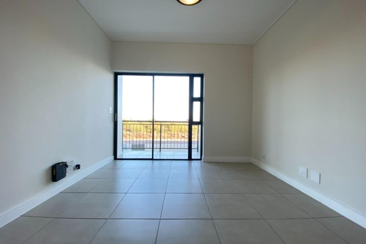 A bright, empty living room featuring large sliding glass doors that open onto a private balcony, finished with neutral floor tiles.